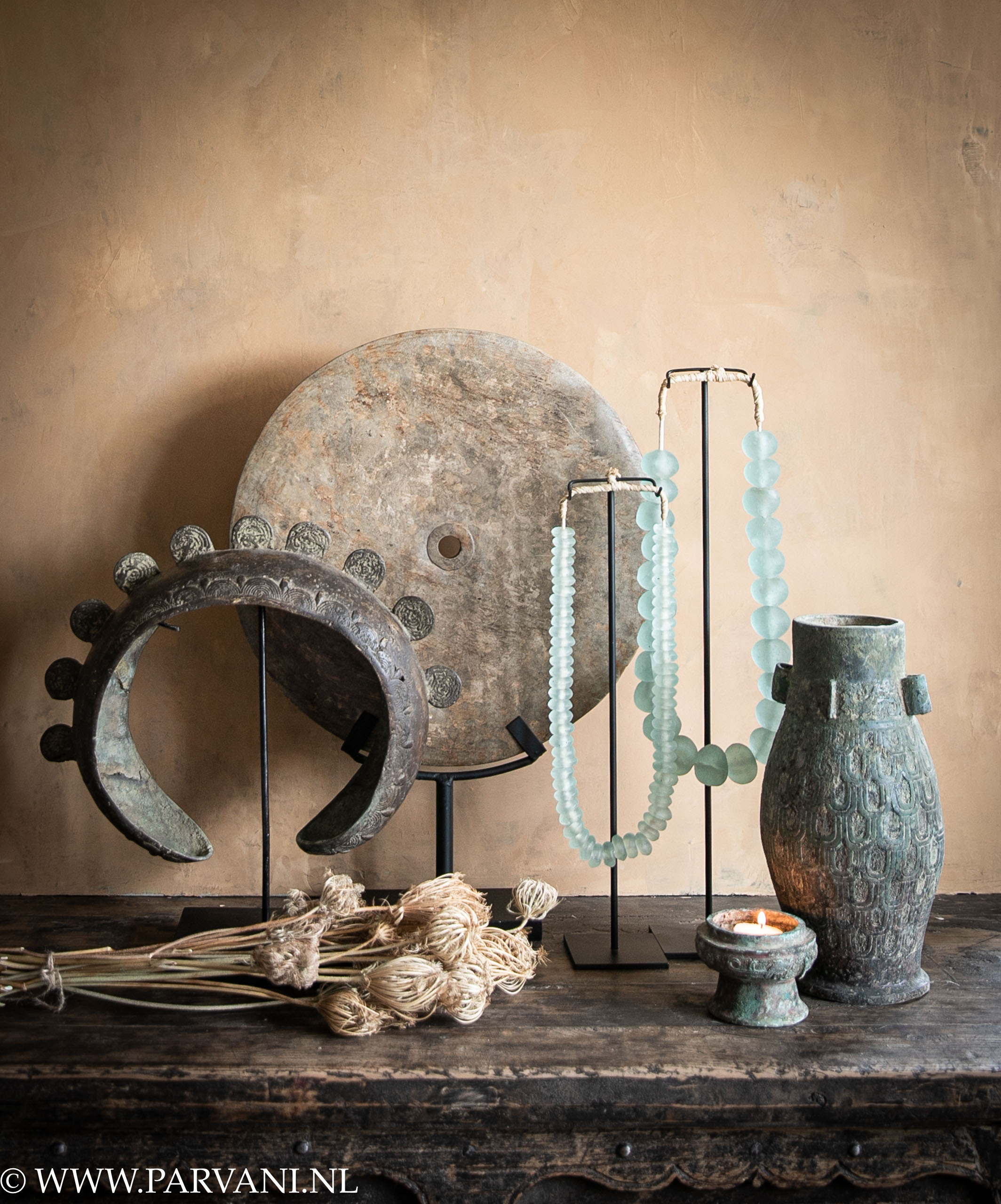ethnische woonaccessoires met stenen schijf en glasketting op standaard en bronzen vaas