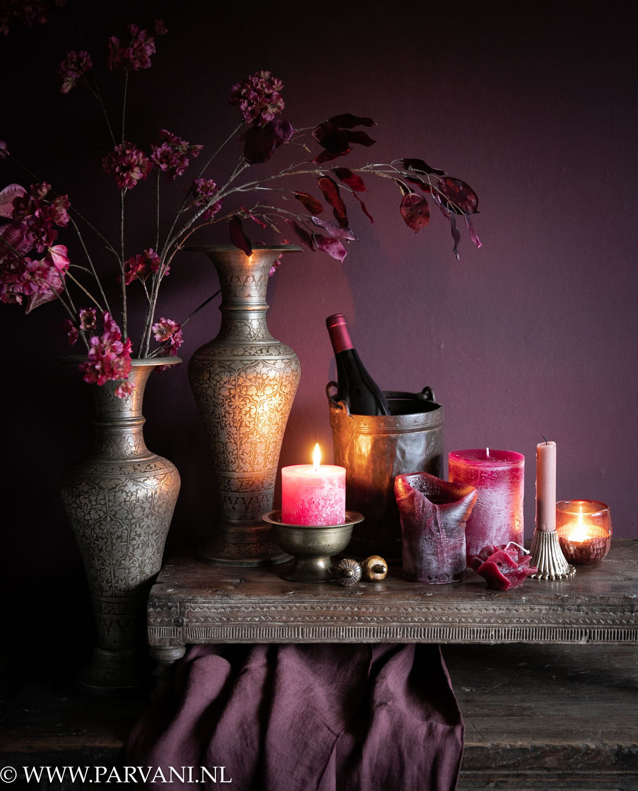 Set oude brass Kaschmiri vazen uit India met zijden bloemen en oude houten bajot tafel met diverse kaarsen, kandelaars en waxinehouders in warme burgundy aubergine kleuren