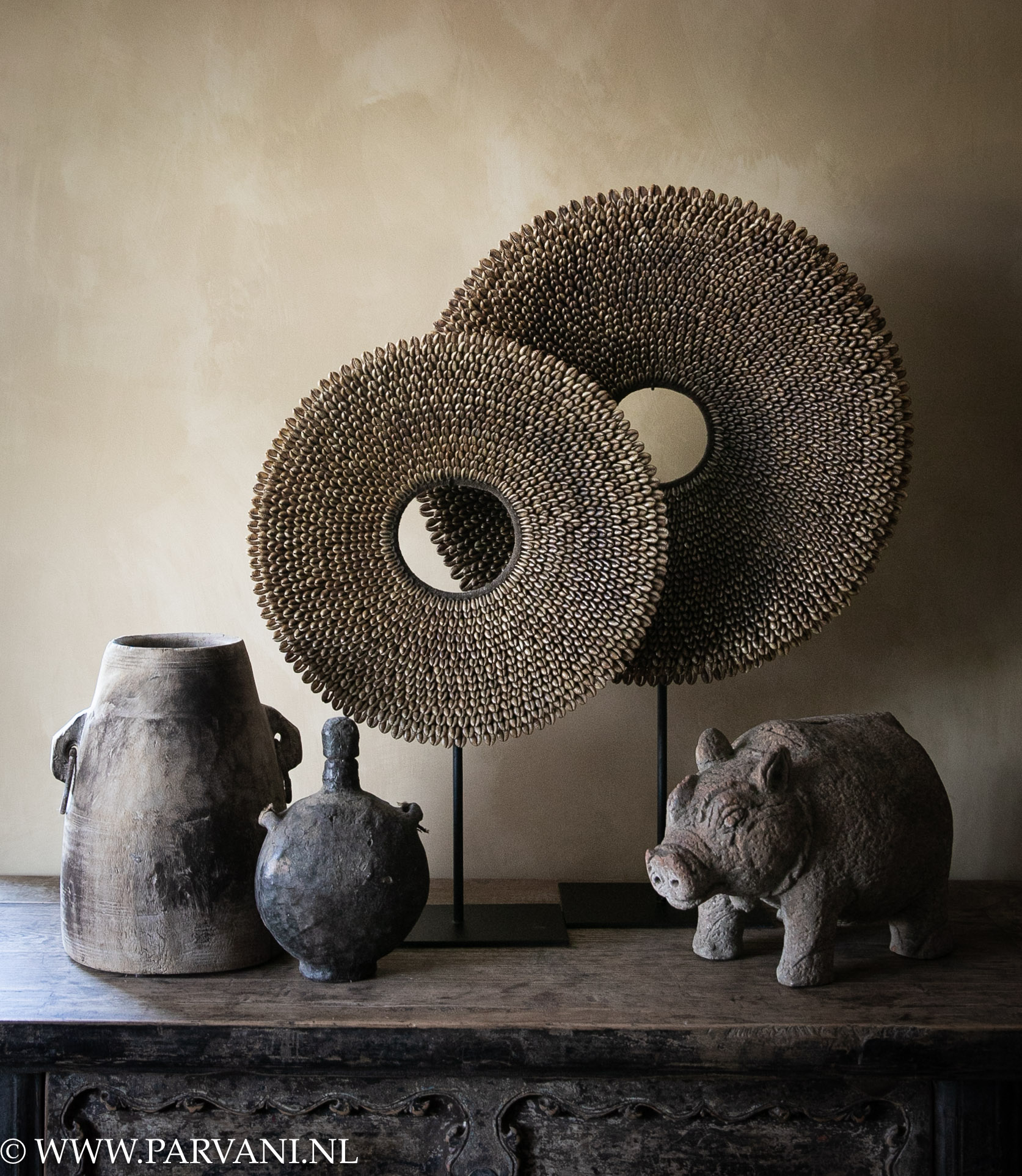 Woonaccessoires in warme bruin aarde kleuren met oud hout, schelpenketting en aardewerk varken en camel fresco muur