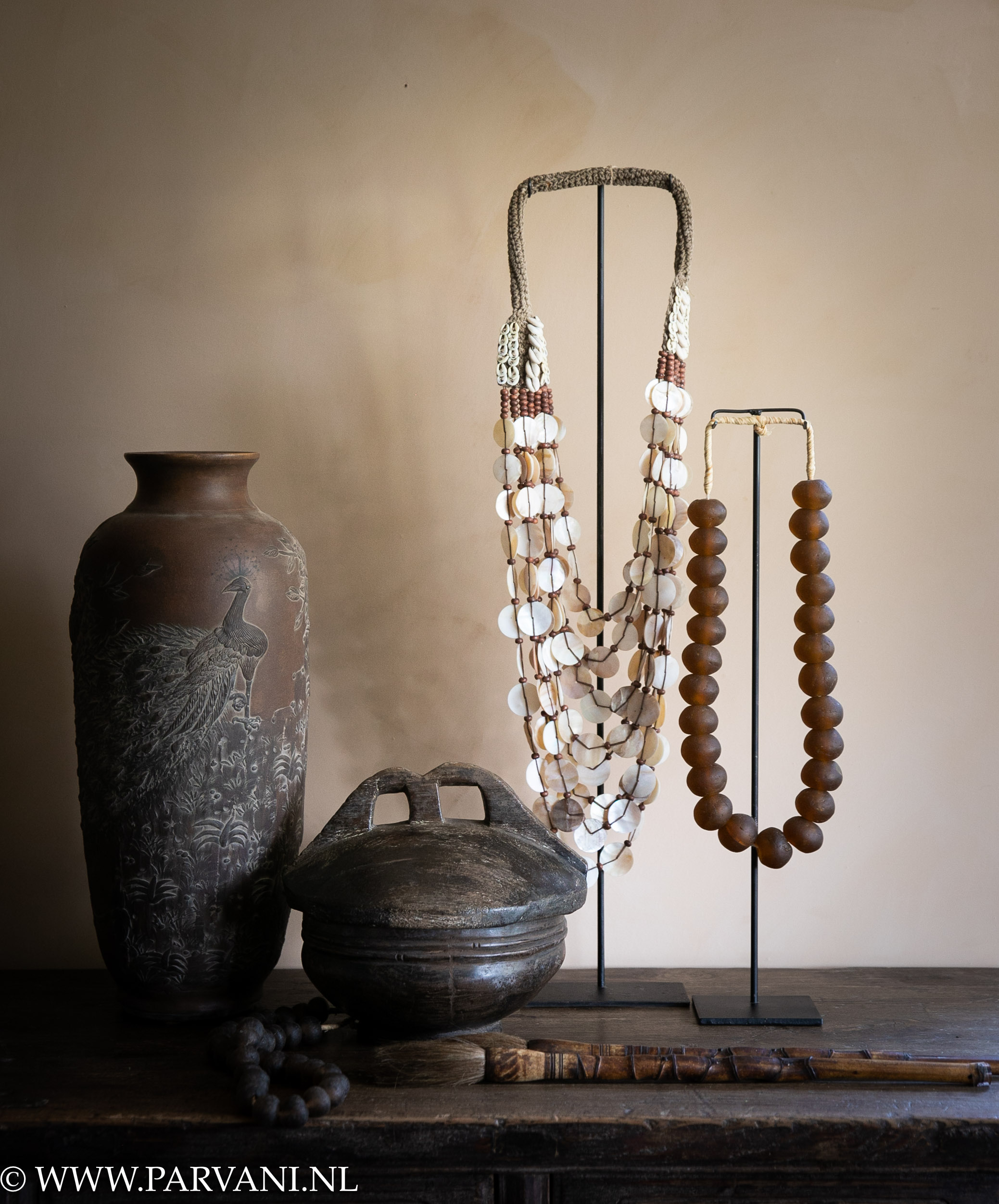 Ethnic woonaccessoires in warme bruine kleuren, oude houten schaal, kettingen op standaard en smalle porseleinen vaas met vogels