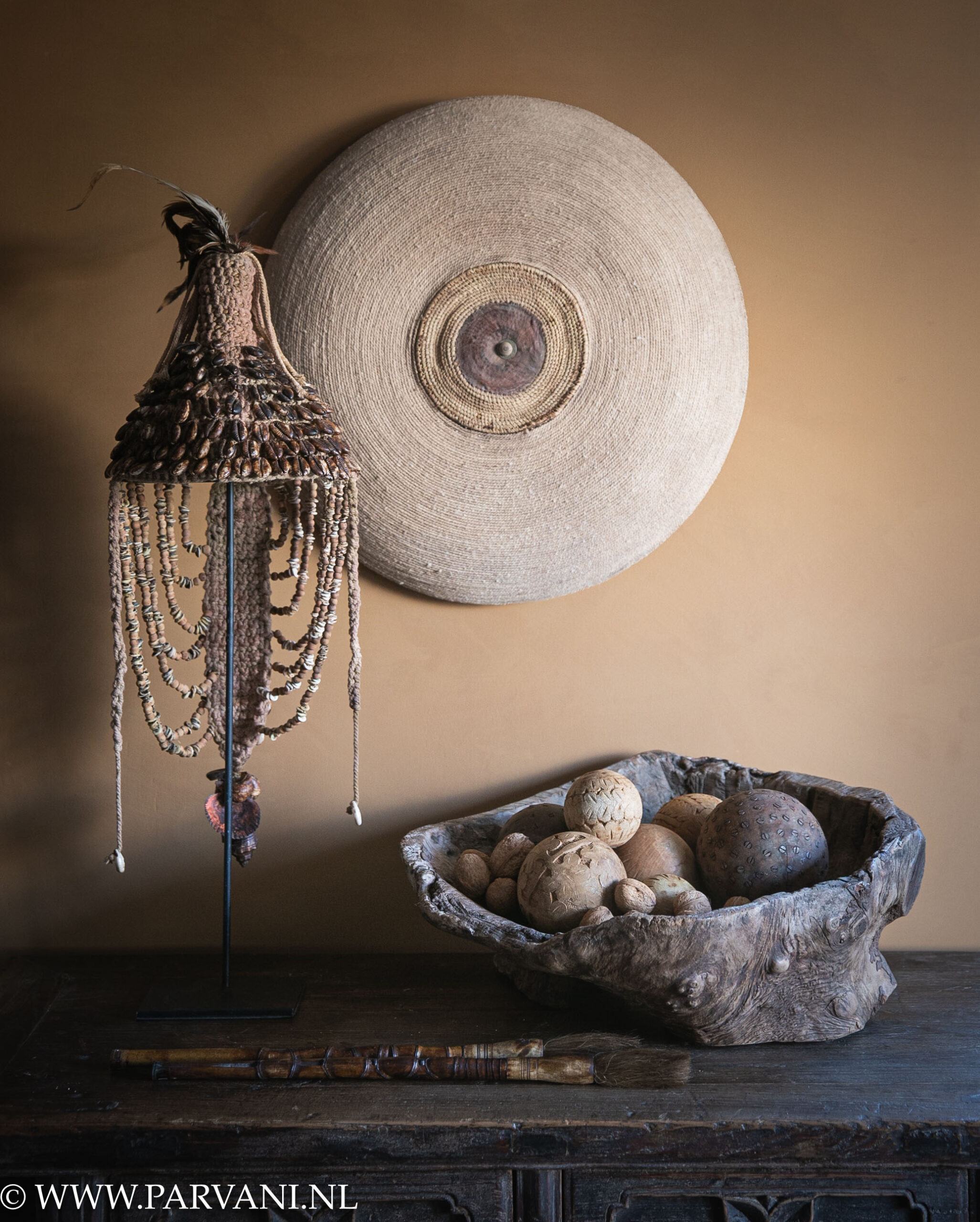 Grillige houten fruitschaal met deco ballen, Indonesisch hoedje met schelpen en kralen op standaard, met Chinese kwasten en groot rond schild met jute en leer