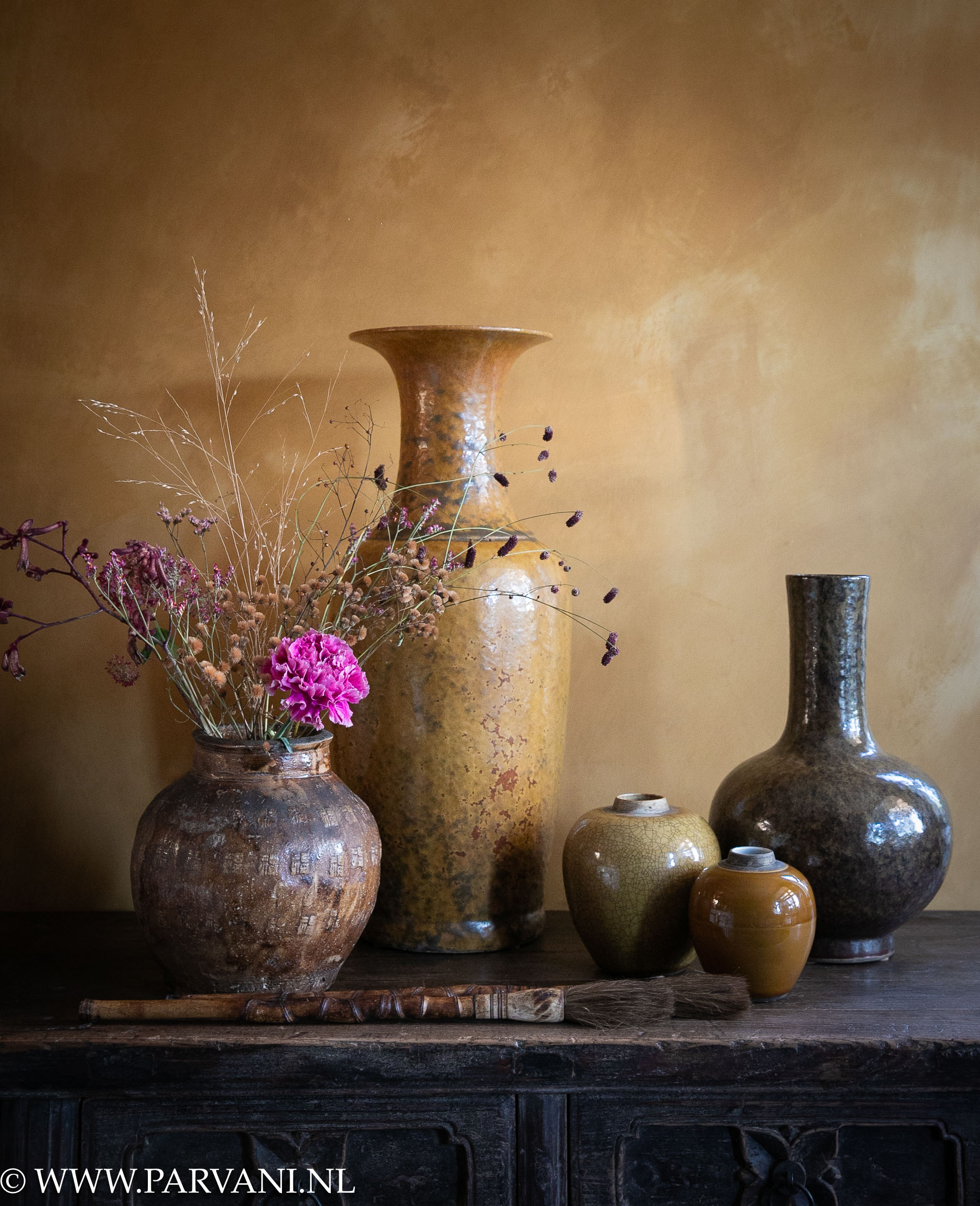 Groepje vazen in oker, mosterdgeel, en groen bruine tinten met bloemen en Chinese kwasten tegen wand in fresco Old Ocre