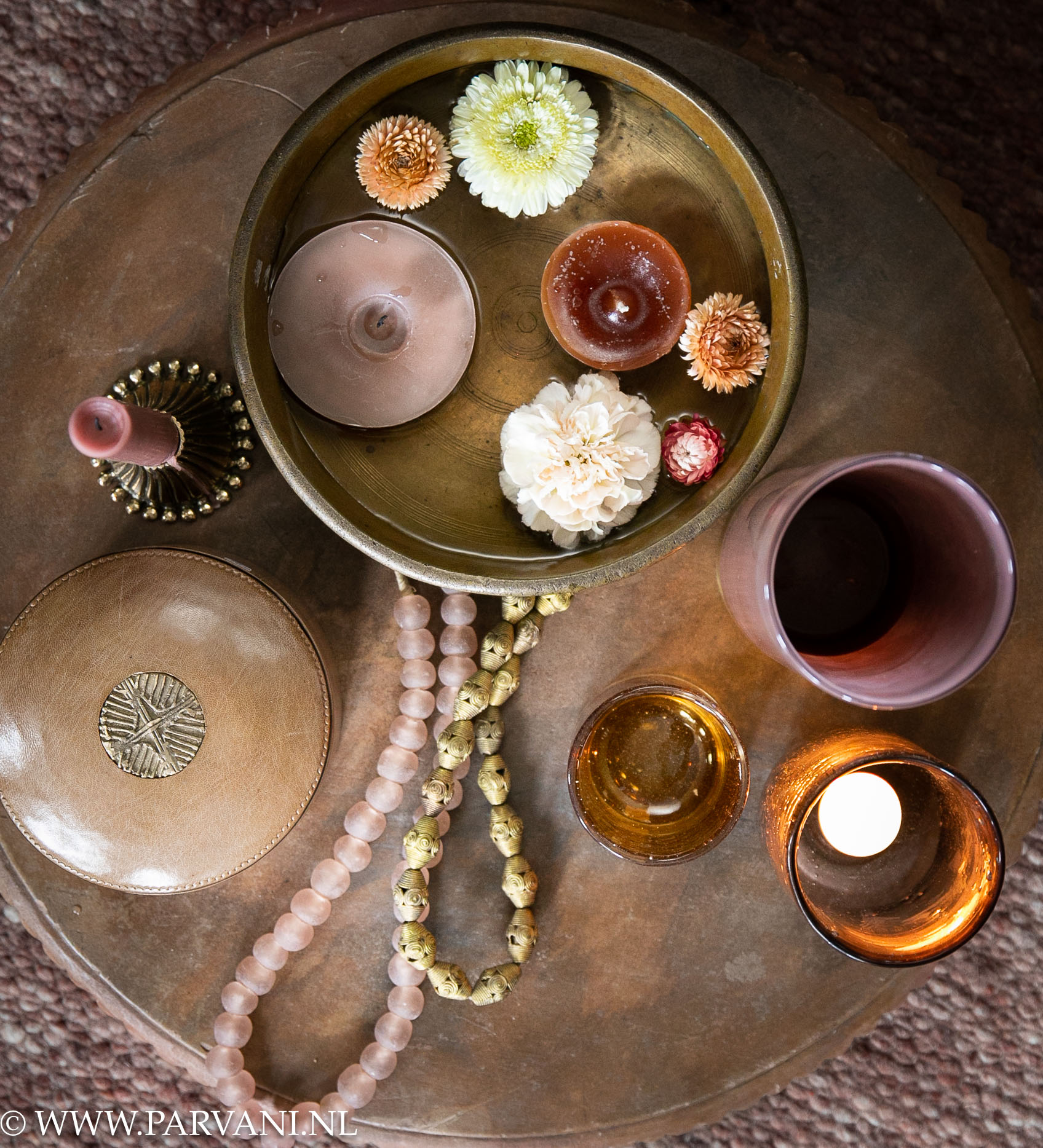 Groot stenen plateau uit India met bronzen uruli, drijfkaarsen en bloemen, met glazen windlichten, messing kandelaar en Afrikaanse kettingen