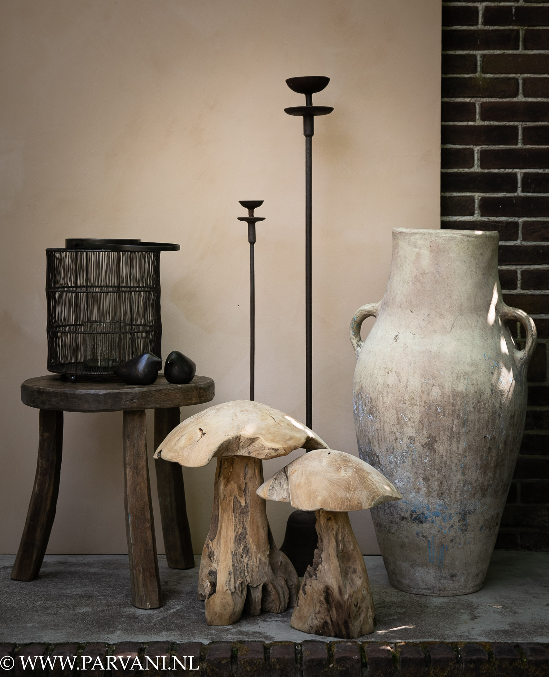 Grote terracotta kruik met houten paddenstoelen en ijzeren kandelaars en windlicht en bronzen vogels