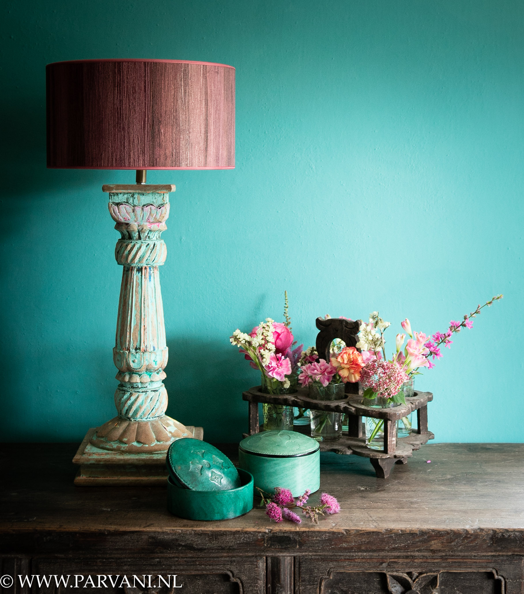 Indiase turquoise blauw roze gekleurde tafellamp met paars roze kap, groene ronde lederen sieradendoosjes en oud rekje met vaasjes bloemen