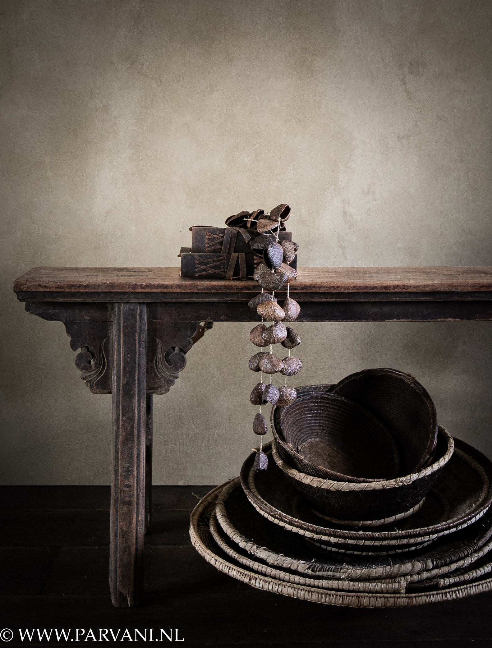 Oud houten bankje uit China met donkerbruine patina en stapel gevlochten Afrikaanse makenge manden