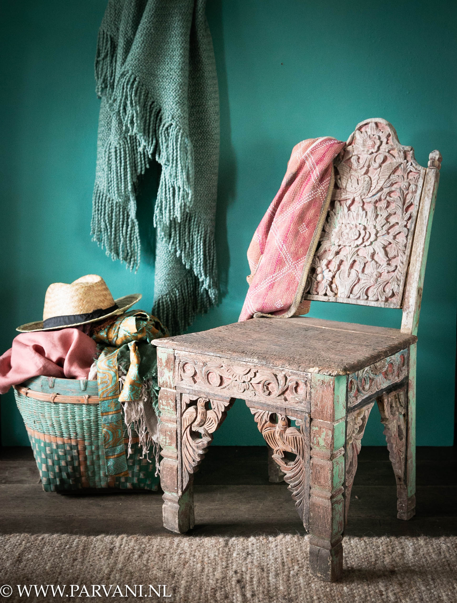 Uniek oud houten stoeltje met houtsnijwerk en roze turquoise kleuren uit Indonesië met groene mand met sjaals en poncho