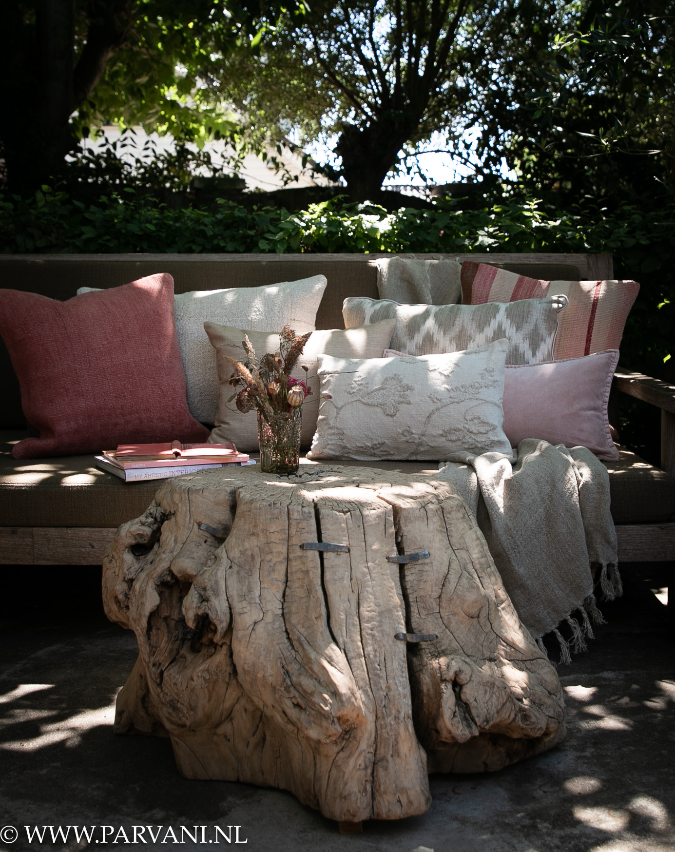 Unieke naturelle lichte boomstam bijzettafel salontafel met organische vorm bij tuinbank met kussens in warme beige roze tinten